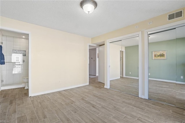 unfurnished bedroom with ensuite bathroom, light hardwood / wood-style floors, multiple closets, and a textured ceiling