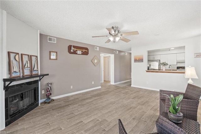 living room featuring light hardwood / wood-style floors, ceiling fan, a textured ceiling, and sink