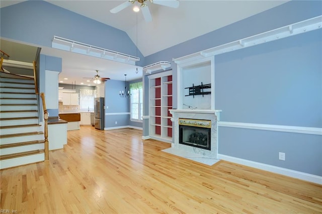 unfurnished living room featuring vaulted ceiling, ceiling fan with notable chandelier, and light wood-type flooring