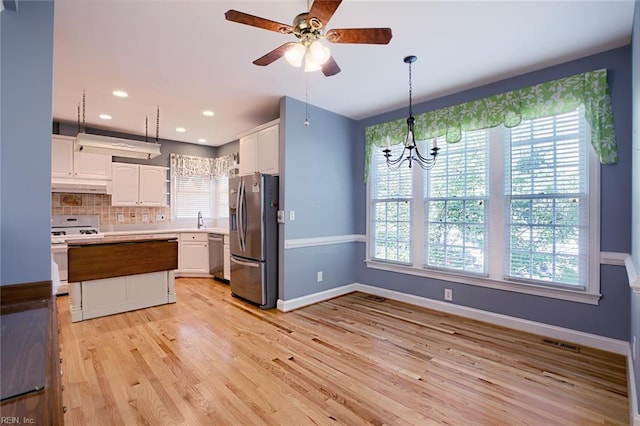 kitchen with pendant lighting, appliances with stainless steel finishes, backsplash, light hardwood / wood-style floors, and white cabinets