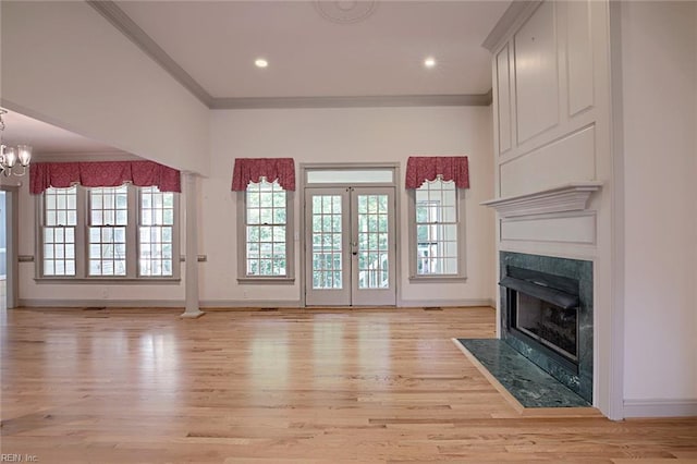 unfurnished living room featuring a high end fireplace, ornamental molding, french doors, a chandelier, and light wood-type flooring