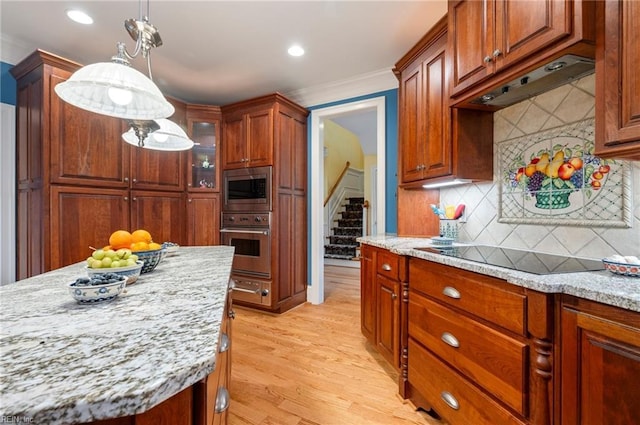 kitchen featuring light stone counters, extractor fan, hanging light fixtures, appliances with stainless steel finishes, and glass insert cabinets