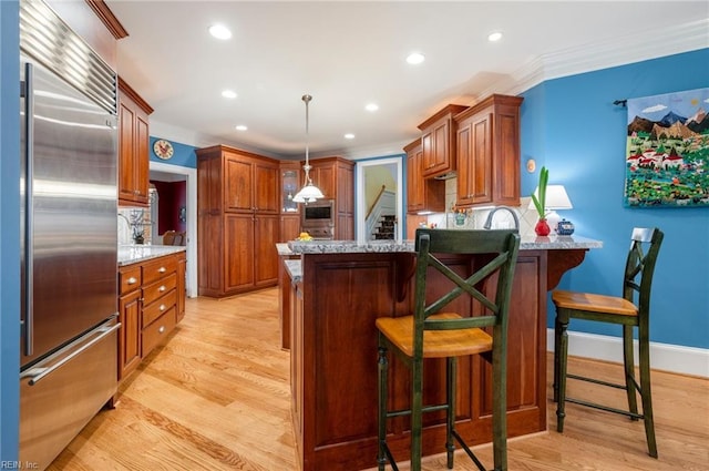 kitchen with brown cabinetry, stainless steel built in fridge, hanging light fixtures, and a breakfast bar area