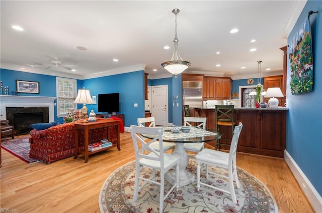 dining space with light wood finished floors, baseboards, ceiling fan, crown molding, and a high end fireplace