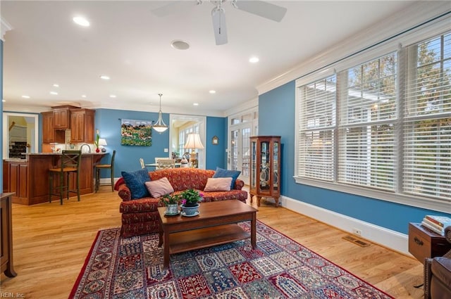 living room featuring light wood-type flooring, a healthy amount of sunlight, crown molding, and baseboards