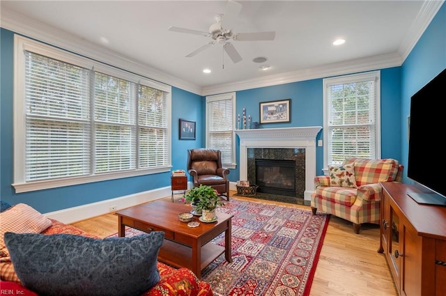 living area featuring baseboards, light wood finished floors, a premium fireplace, and crown molding