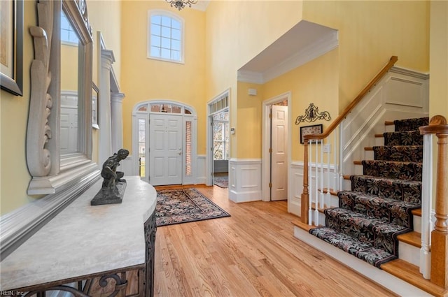 foyer entrance with light wood-style floors, stairway, a decorative wall, and wainscoting