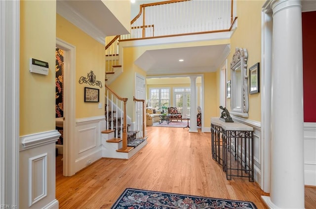 foyer featuring wainscoting, crown molding, light wood finished floors, and ornate columns