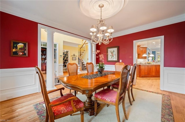 dining area featuring light wood-type flooring, wainscoting, ornate columns, and stairs