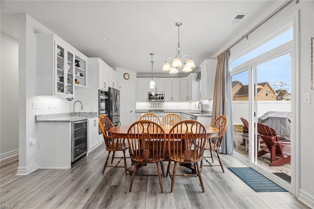 dining space with sink, a chandelier, beverage cooler, and light hardwood / wood-style floors