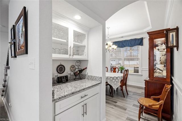 bar with white cabinetry, light stone countertops, a notable chandelier, and light hardwood / wood-style flooring