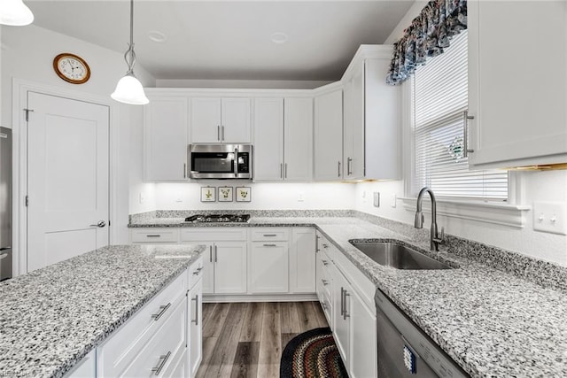 kitchen featuring sink, appliances with stainless steel finishes, white cabinetry, hardwood / wood-style floors, and hanging light fixtures