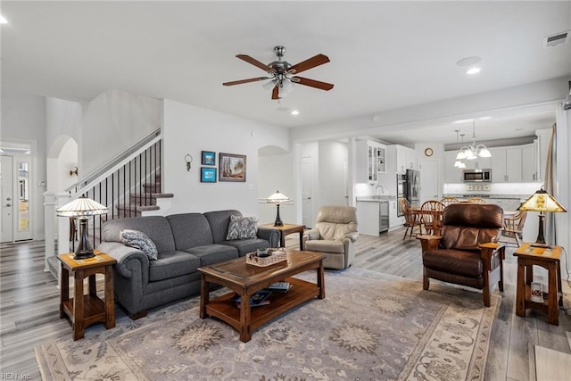 living room with ceiling fan with notable chandelier and light hardwood / wood-style flooring