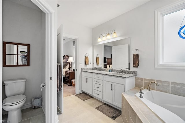 bathroom with a relaxing tiled tub, vanity, toilet, and tile patterned flooring