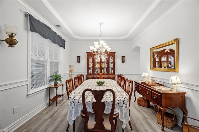 dining space featuring a raised ceiling, ornamental molding, an inviting chandelier, and light wood-type flooring