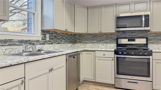 kitchen with tasteful backsplash, appliances with stainless steel finishes, light stone countertops, and sink