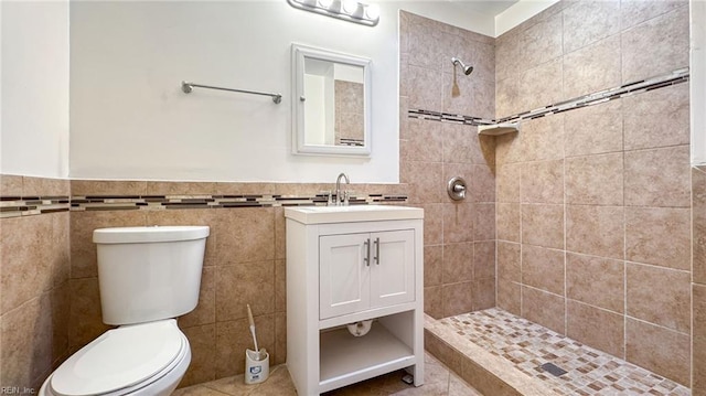 bathroom with vanity, tile walls, toilet, and tiled shower