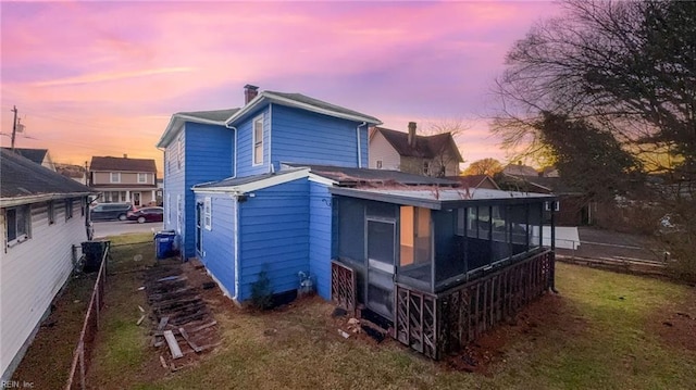 back house at dusk with a lawn and a sunroom