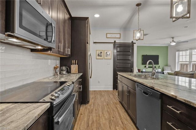 kitchen with pendant lighting, appliances with stainless steel finishes, dark brown cabinetry, light stone counters, and a barn door