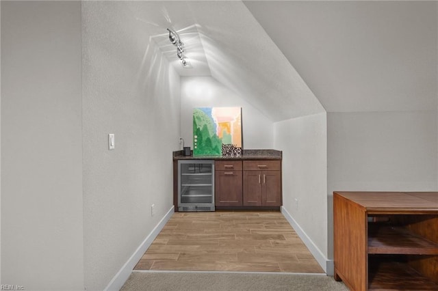 bar featuring wine cooler, track lighting, lofted ceiling, and light wood-type flooring