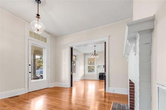 foyer entrance featuring an inviting chandelier, a wealth of natural light, crown molding, and light wood-type flooring