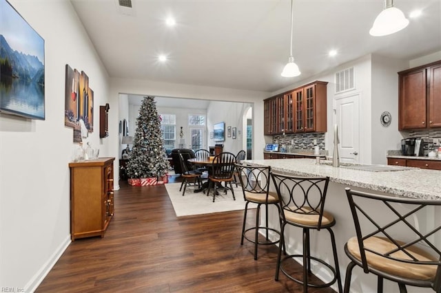 kitchen with light stone countertops, dark hardwood / wood-style floors, decorative backsplash, and decorative light fixtures