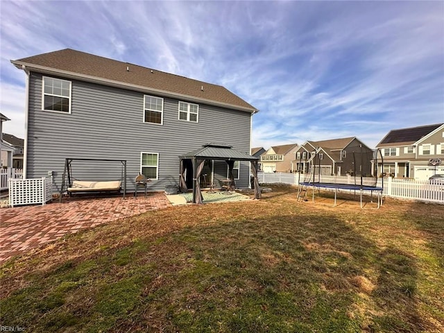 rear view of property featuring a trampoline, a lawn, a patio area, and a gazebo