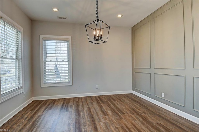 unfurnished dining area featuring a healthy amount of sunlight, dark hardwood / wood-style flooring, and a notable chandelier