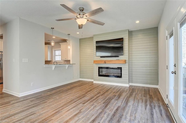 unfurnished living room featuring hardwood / wood-style floors, sink, a large fireplace, and ceiling fan