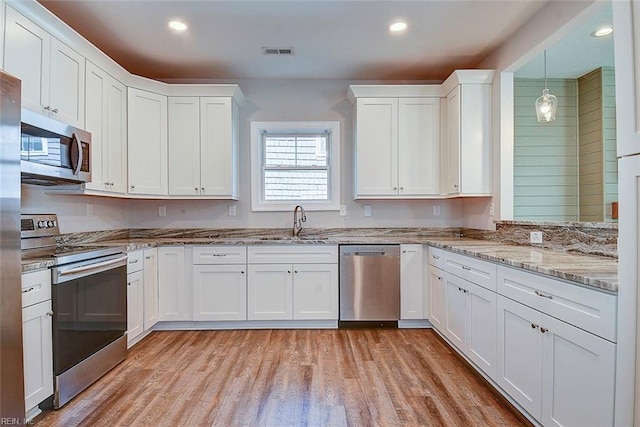 kitchen featuring sink, white cabinetry, hanging light fixtures, light hardwood / wood-style flooring, and stainless steel appliances