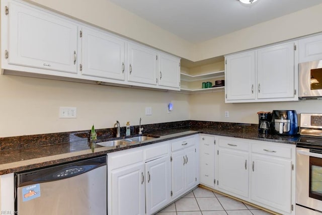 kitchen with sink, light tile patterned floors, appliances with stainless steel finishes, white cabinetry, and dark stone countertops