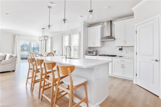 kitchen with sink, white cabinetry, an island with sink, decorative light fixtures, and wall chimney exhaust hood