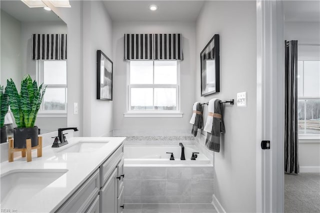 bathroom featuring a wealth of natural light, vanity, and tiled tub