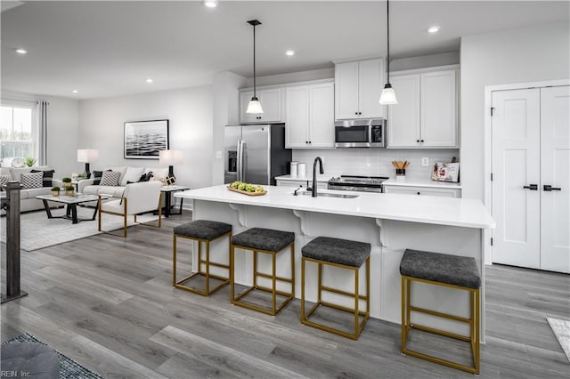 kitchen with a center island with sink, a kitchen bar, appliances with stainless steel finishes, and decorative light fixtures