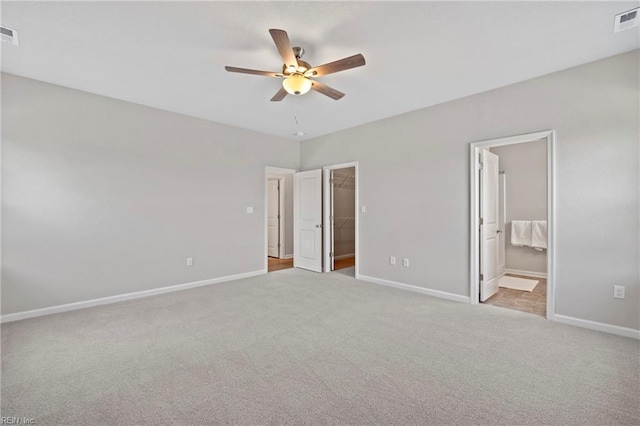 unfurnished bedroom with ceiling fan, light colored carpet, a closet, and a walk in closet