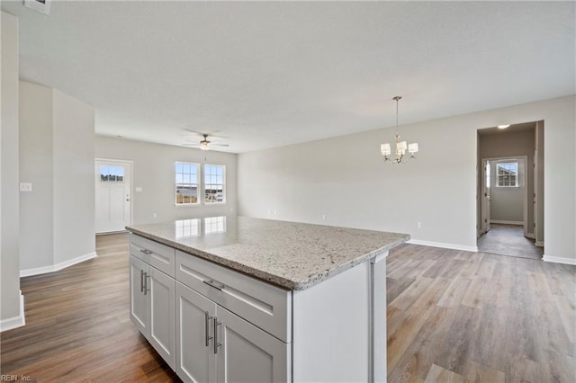 kitchen with light stone counters, light hardwood / wood-style flooring, a kitchen island, pendant lighting, and ceiling fan with notable chandelier