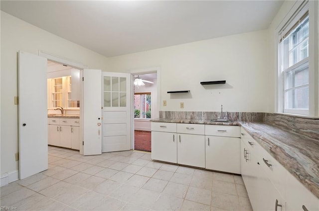 kitchen featuring stone counters, sink, light tile patterned floors, and white cabinets