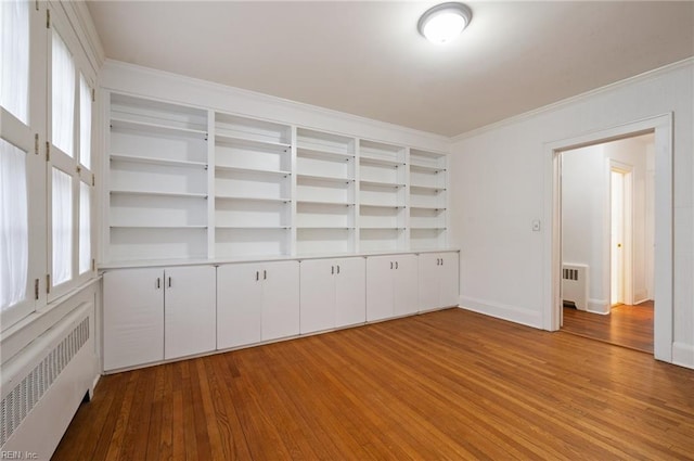 unfurnished room featuring crown molding, radiator, light hardwood / wood-style floors, and built in shelves