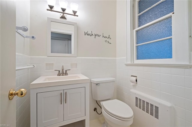 bathroom with radiator heating unit, toilet, vanity, and tile walls