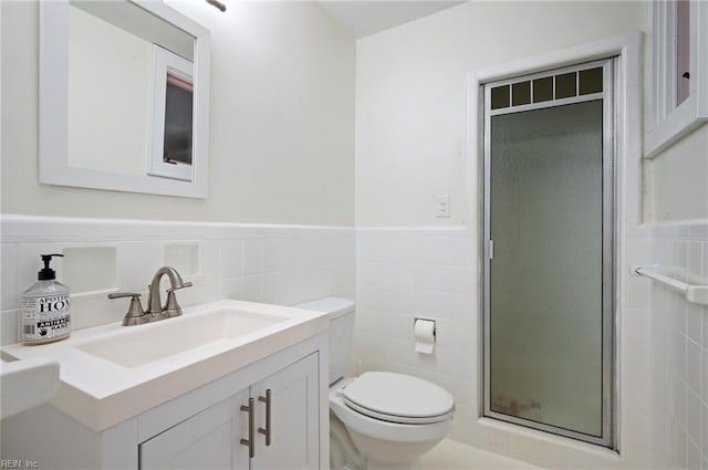 bathroom with vanity, a shower with door, tile walls, and toilet