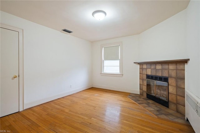 unfurnished living room with a tiled fireplace, radiator, and light hardwood / wood-style floors