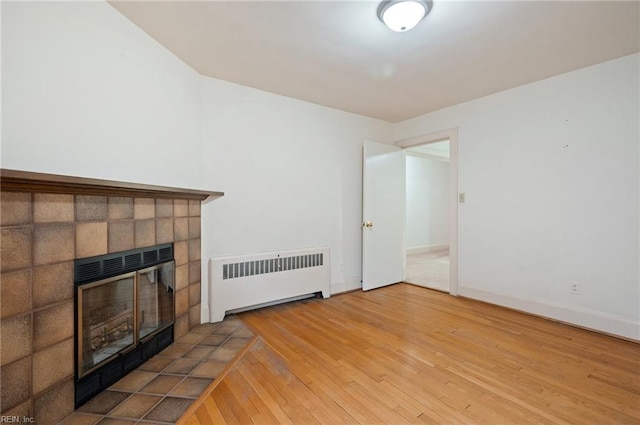 unfurnished living room featuring hardwood / wood-style flooring, a tile fireplace, and radiator heating unit