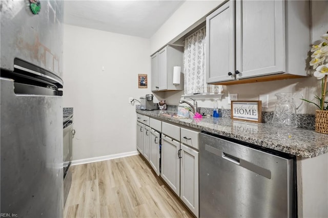 kitchen featuring light stone countertops, sink, stainless steel dishwasher, and light hardwood / wood-style flooring