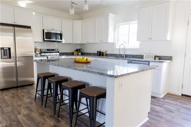 kitchen with a breakfast bar, appliances with stainless steel finishes, white cabinetry, ornamental molding, and a kitchen island