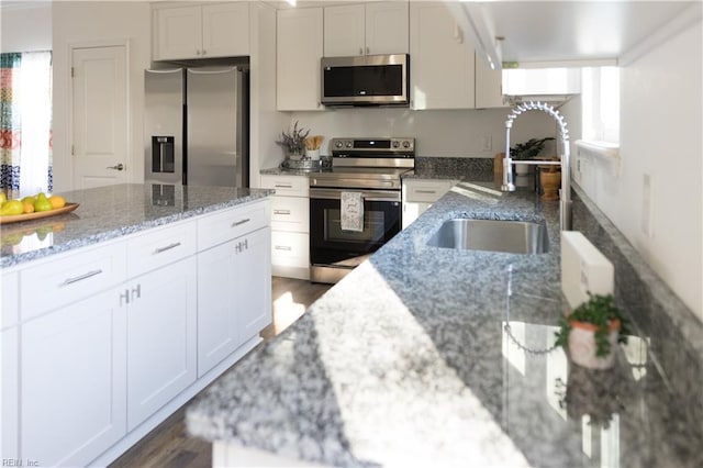 kitchen featuring sink, appliances with stainless steel finishes, white cabinetry, hardwood / wood-style floors, and light stone counters