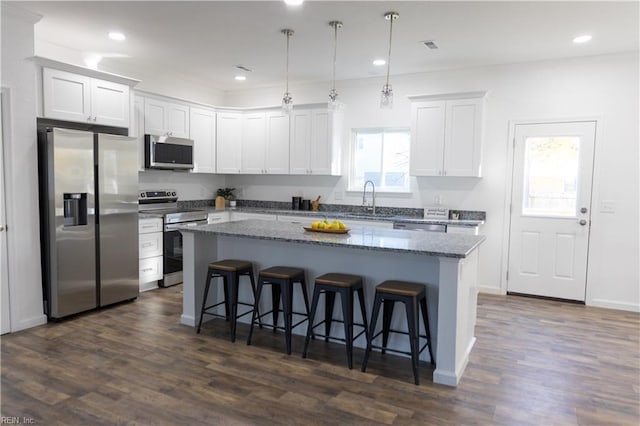 kitchen featuring a center island, dark stone countertops, pendant lighting, stainless steel appliances, and white cabinets