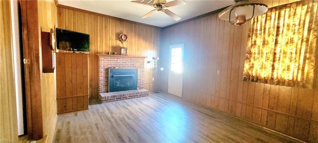 unfurnished living room featuring wood-type flooring, ornamental molding, wooden walls, ceiling fan, and a fireplace