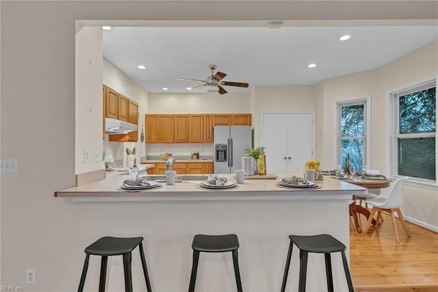 kitchen featuring stainless steel refrigerator with ice dispenser, a kitchen bar, light hardwood / wood-style flooring, kitchen peninsula, and ceiling fan