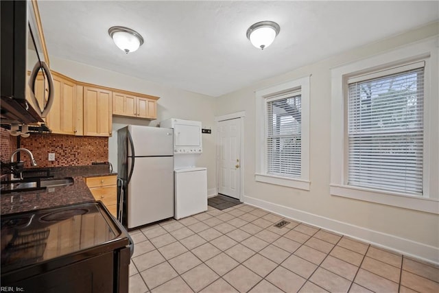 kitchen featuring stacked washing maching and dryer, light brown cabinetry, sink, decorative backsplash, and fridge