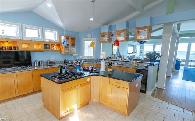 kitchen featuring wine cooler, decorative columns, an island with sink, and stainless steel gas cooktop